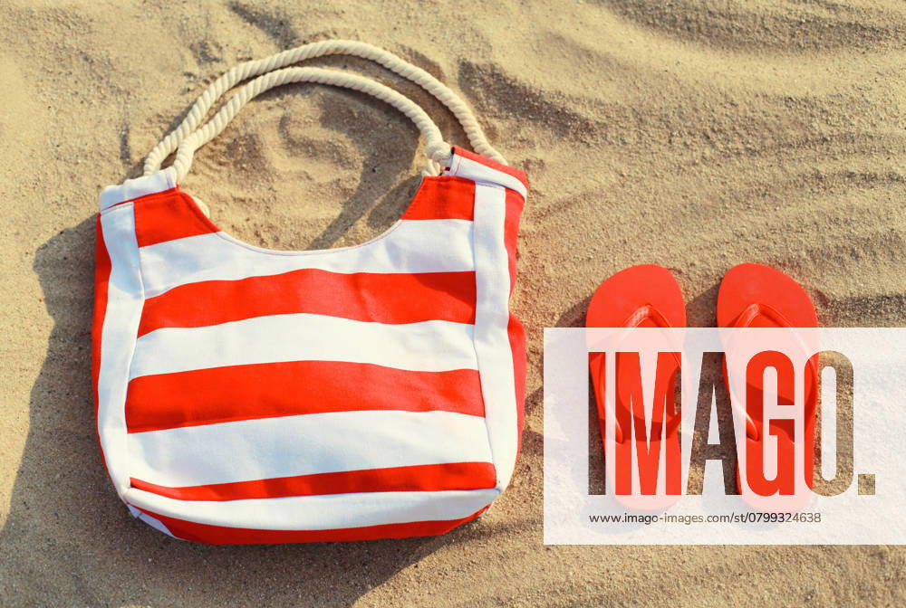 Sommerurlaub, Accessoires - rot gestreifte Tasche mit Flip Flops im Sand am Strand Summer vacation, accessories - red striped bag with flip flops lying on the sand on the beach, top view