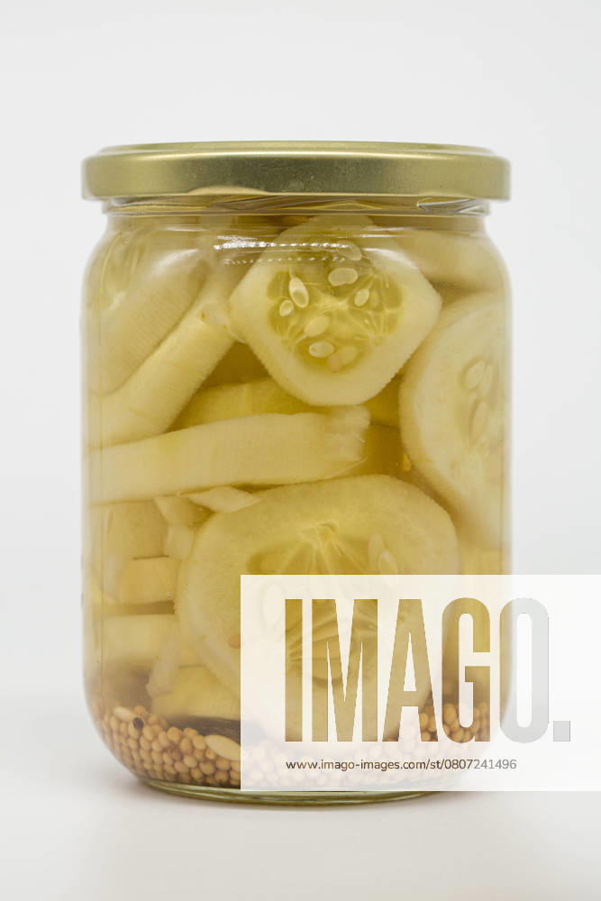 A glass jar filled with sliced pickled cucumbers immersed in vinegar, showcasing mustard seeds at the bottom. Perfect for illustrating food preservation or homemade pickling. Model Released LauraZamora_ID26925_776983_017
