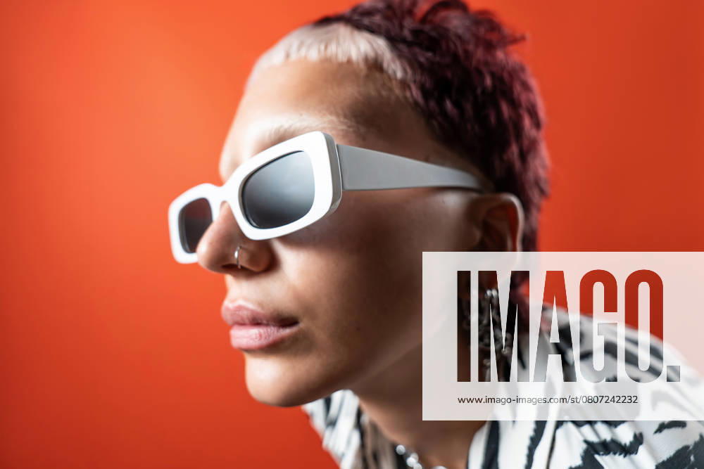 Close-up of a fashion model wearing white sunglasses and zebra animal print attire, set against a vibrant orange backdrop. The studio flash photography creates a striking and modern look. Model Released ManuelRuiz_ID27375_785302_009