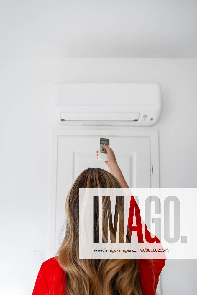 IMAGO Creative, Jahreszeit Sommer, Hitze Frau mit Fernbedienung, die auf die Klimaanlage gerichtet ist. Woman holding remote control aimed at the air conditioner. (License=RF) ,model released, Symbolfoto