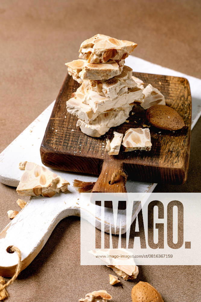 Spanischer Dessert-Klassiker Turron Traditional Spanish dessert classic crunchy turron with almonds, broken into pieces on wooden serving board. Beige textured background. (License=RF)