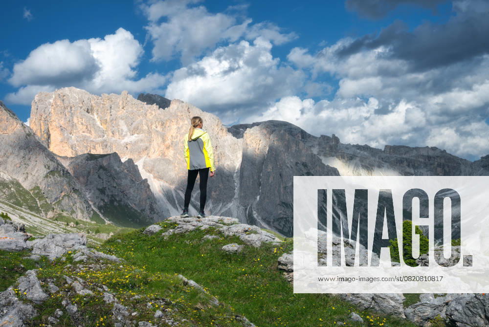 Girl on the hill with yellow flowers and green grass in beautiful alpine mountain valley at sunset in summer. Landscape with young woman in alps, sky with clouds, rocks. Travel in Dolomites, Italy Model Released DenisBilytskyi_ID26964_778295_016