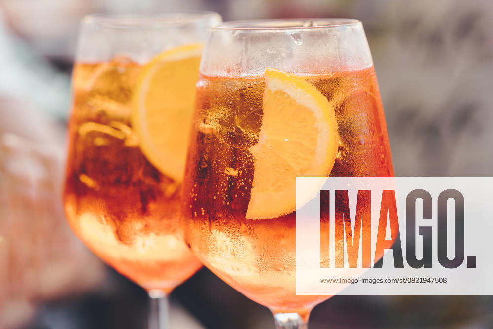 Ein Glas eiskalter Aperol Spritz-Cocktail, serviert in einem Weinglas, verziert mit Orangenspalten. Aperitif im Straßencafé Glass of ice cold Aperol spritz cocktail served in a wine glass, decorated with slices of orange. Aperitif in street caffe in Italy (License=RF)