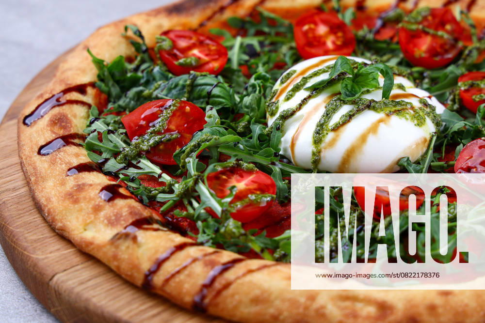 Burrata Arugula Pizza with Cherry Tomatoes Pesto and Balsamic Drizzle Artisan pizza topped with creamy burrata, fresh arugula, cherry tomatoes, pesto and balsamic drizzle. (License=RF)