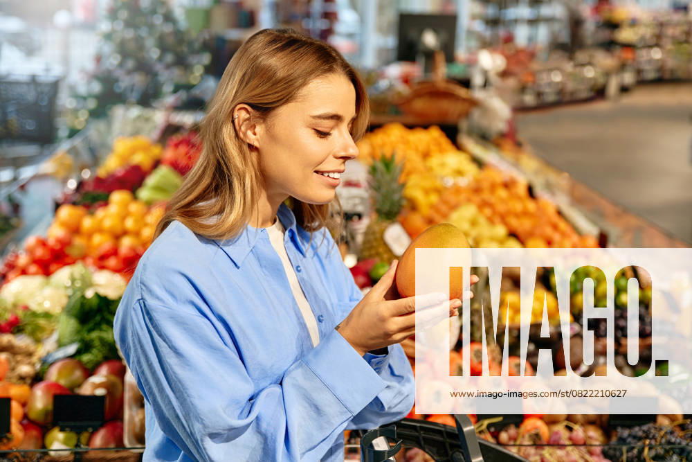 Woman enjoying the scent of ripe mango at fruit market Young woman smiling while holding and smelling a ripe mango in a vibrant supermarket produce section. Concept of healthy lifestyle, fresh tropical fruits, and sensory enjoyment of food. Model Released OrionProduction_ID29903_1009870_074