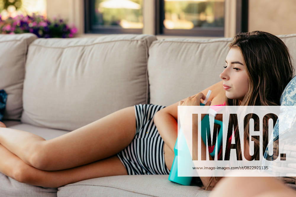 IMAGO Creative, Jahreszeit Sommer, Hitze Young woman relaxing on sofa with cold drink on summer day Boise, Idaho, United States CR_PHZD250620B-1767956-01 ,model released, Symbolfoto