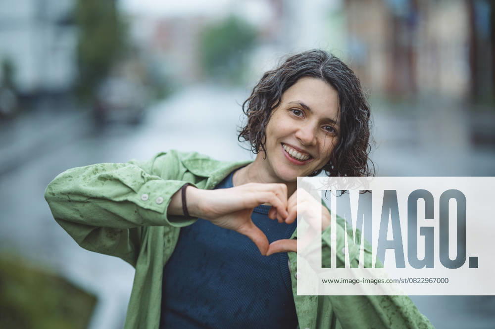 Smiling woman making heart symbol in city on rainy day model released, Symbolfoto, ANAF04798