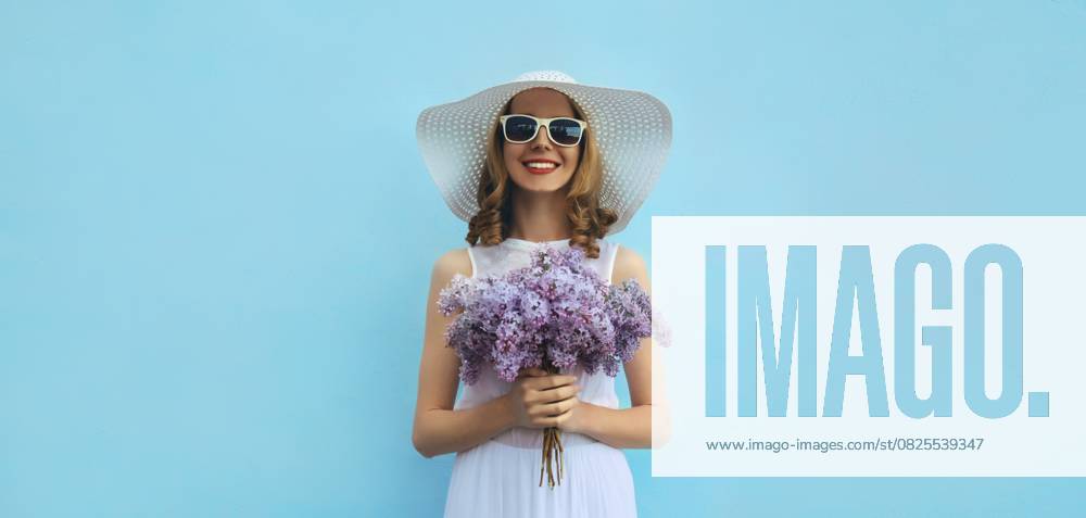 Sommer Porträt der schönen schönen glücklich lächelnde Frau mit Blumenstrauß von lila Flieder Blumen in weißen Strohhut auf blauem Hintergrund Summer portrait of beautiful lovely happy smiling woman with bouquet of purple lilac flowers in white straw hat on blue background