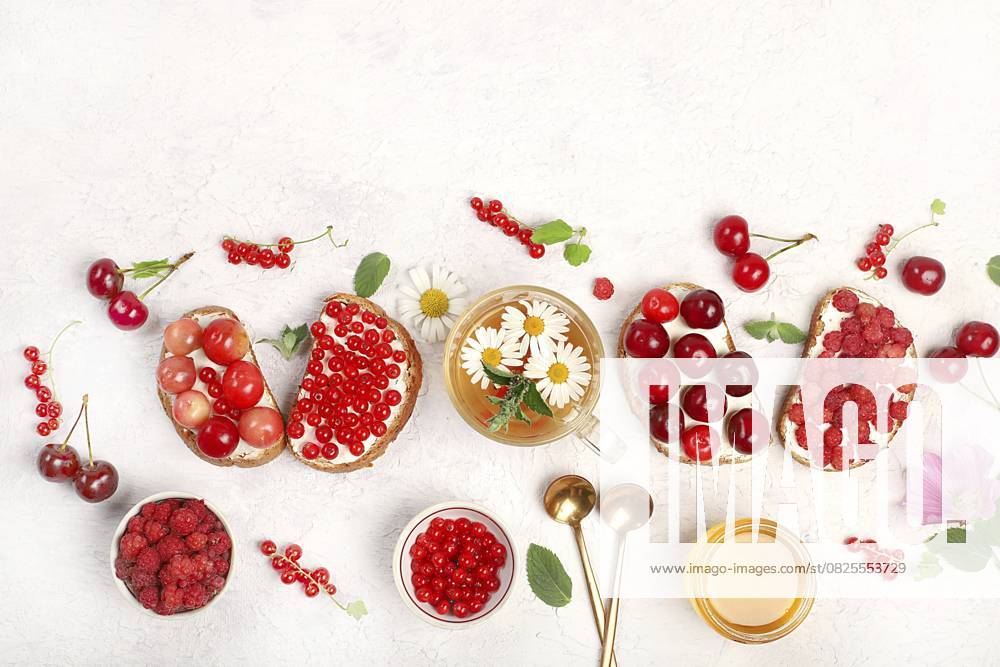 Gesundes Frühstück mit Zutaten und Kräutertee mit Kamille. Diät Obst Mini Sandwiches mit weichem Hüttenkäse und frischen Beeren, Himbeeren, Johannisbeeren und Kirschen, Das Konzept der gesunden und natürlichen Ernährung, Lebensstil, flat lay, Platz für Text, selektiver Fokus Healthy breakfast with ingredients and herbal tea with chamomile. Diet fruit mini sandwiches with soft cottage cheese and fresh berries, raspberries, currants and cherries, The concept of healthy and natural food, lifestyle, flat lay, space for text, selective focus
