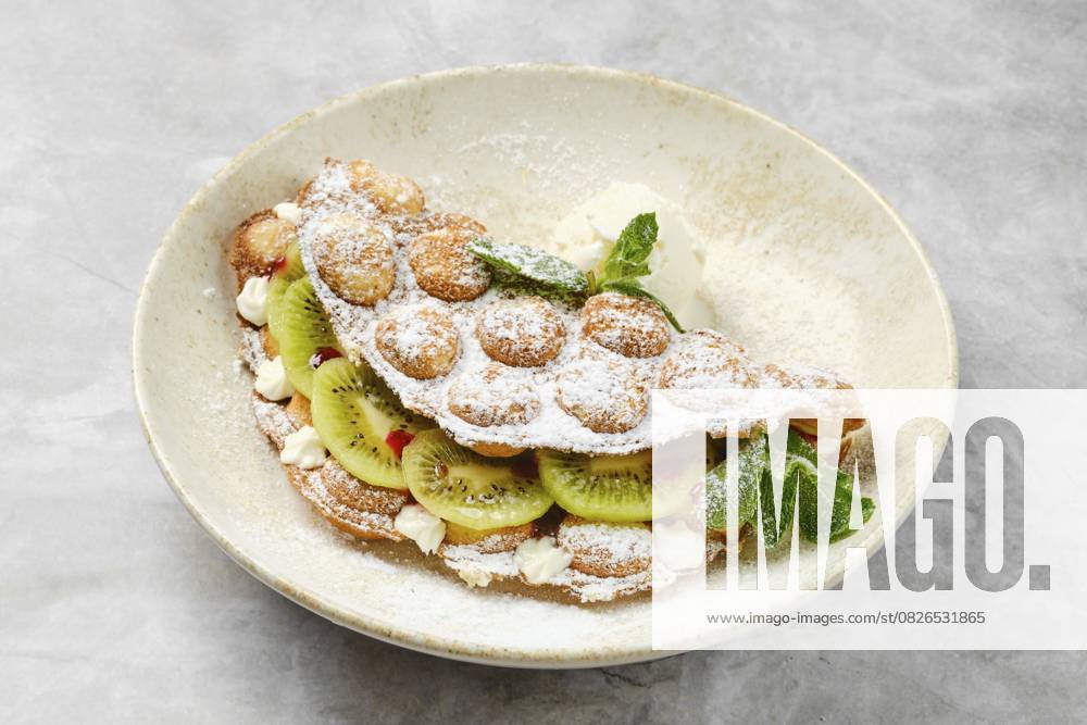 Ein köstliches Dessert mit einer fluffigen Schale, gefüllt mit frischen Kiwischeiben und Schlagsahne, dekoriert mit etwas Puderzucker und einem Hauch von Minze. Perfekt für eine süße Leckerei A delightful dessert showcases a fluffy shell filled with fresh kiwi slices and whipped cream, decorated with a sprinkle of powdered sugar and a touch of mint. Perfect for a sweet treat