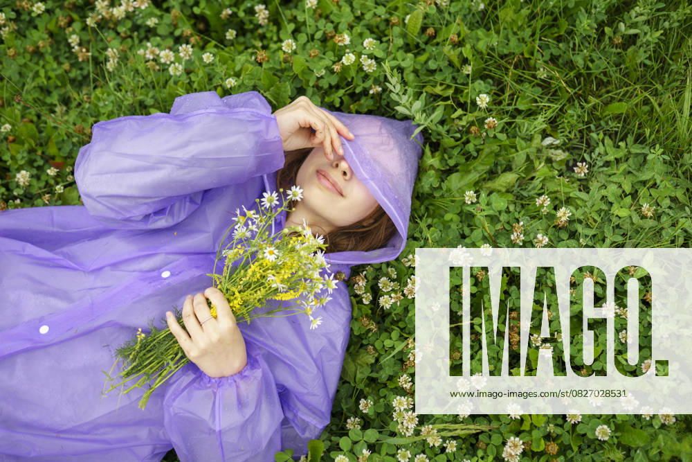 Creative Highlight Symbolbilder Woman in purple raincoat relaxing on grass with wild flowers in summer model released, Symbolfoto, VCF00802