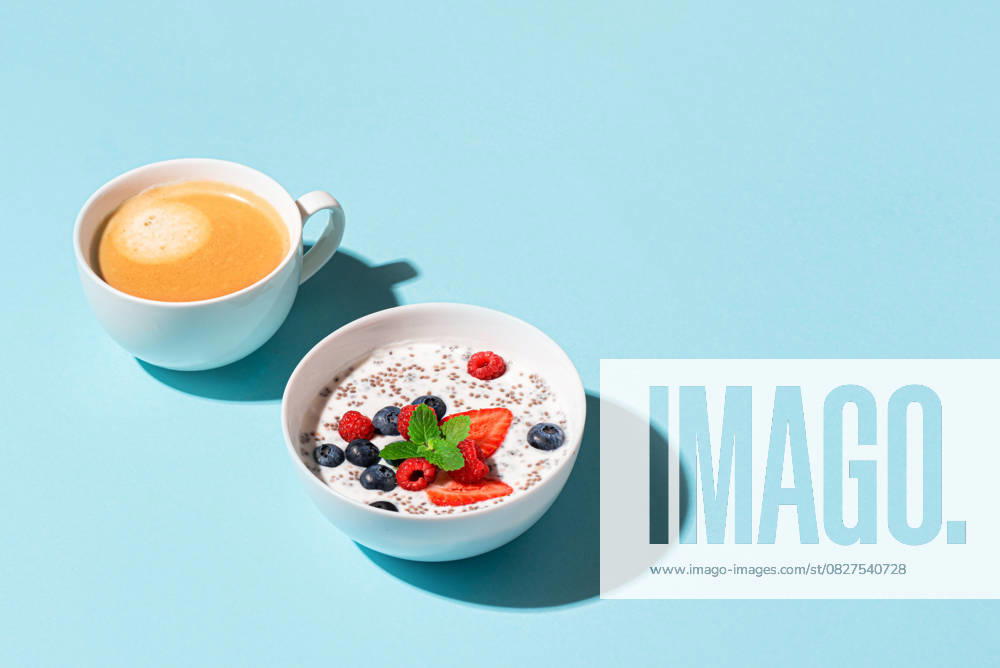 IMAGO Creative, Food, High Protein Frühstück Gesundes Frühstück mit Chia-Schale und Cappuccino-Kaffee auf blauem Hintergrund, trendiges Design mit hartem Licht. Chia-Pudding mit Beeren. Gesunde pflanzenbasierte Ernährung, Fitness Sommer Rezept. Healthy breakfast with chia bowl and cappuccino coffee on blue background, trendy design with hard light. Chia pudding with berries. Healthy plant based diet, fitness summer recipe. (License=RF)