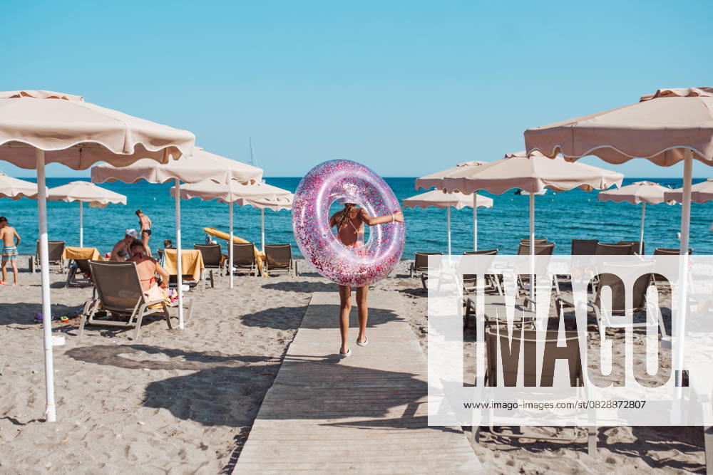 Rear view of girl walking to the beach with swim ring. summer beach holiday. Rear view of girl walking to the beach with swim ring in hand. Summer beach holiday. model released