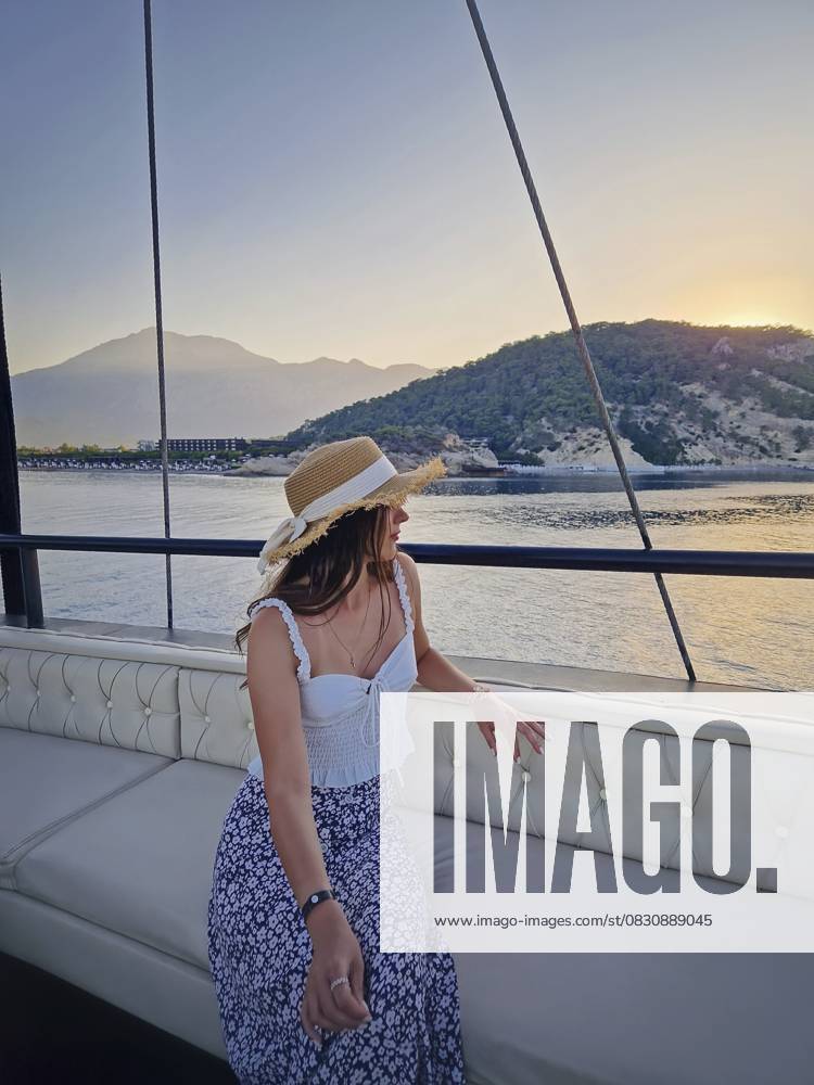Junge Frau Tourist trägt Strohhut, Segeln auf einem Boot Blick auf die Kiris Resort Küste in der Türkei. Frau genießt die Aussicht beim Segeln auf dem tiefblauen Mittelmeer Young woman tourist wearing straw hat, sailing on a boat gazing out the Kiris resort coastline in Turkey. Female enjoying the views as cruising on the deep blue Mediterranean Sea