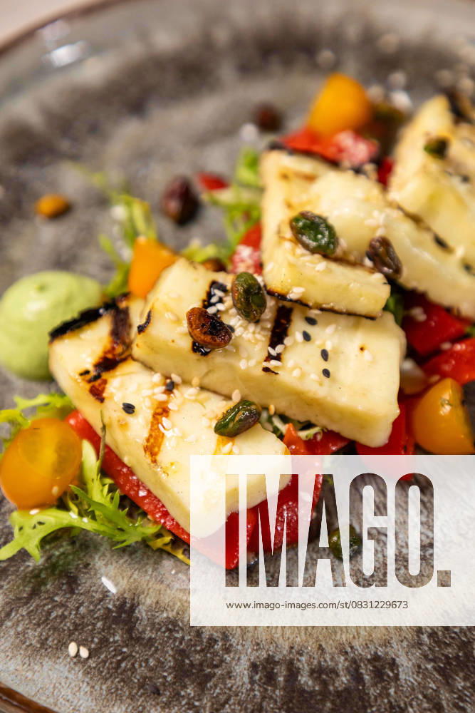 Delicious grilled halloumi cheese salad with a side of pesto sauce Grilled halloumi cheese salad with cherry tomatoes and pistachios being served on a plate, 63074770.jpg RECORD DATE NOT STATED
