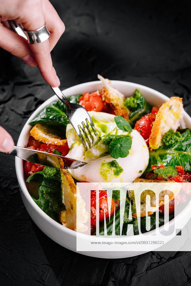 Frischer Burrata-Käse-Salat mit Tomaten und Spinat Bowl of burrata cheese salad, with ripe tomatoes, spinach, and crispy bread on black background (License=RF)