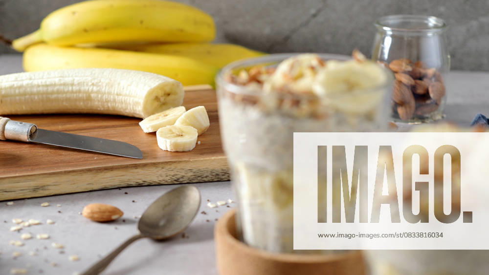IMAGO Creative, Food, High Protein Frühstück Two bowls of overnight oats topped with banana slices and almonds Two bowls of overnight oats topped with banana slices and almonds. A spoon, cutting board, knife, and a blue napkin rest nearby., 63441024.jpg RECORD DATE NOT STATED