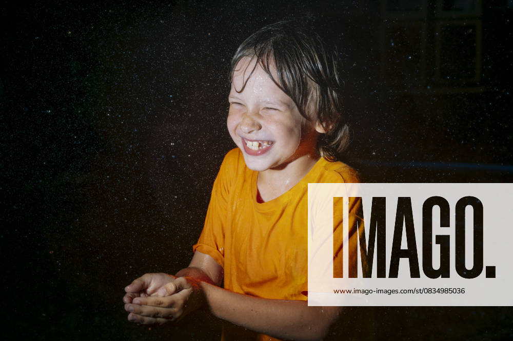 IMAGO Creative, Jahreszeit Sommer, Regen, Sommerregen Smiling child in orange shirt playing in rain at night model released, Symbolfoto, ANAF05001