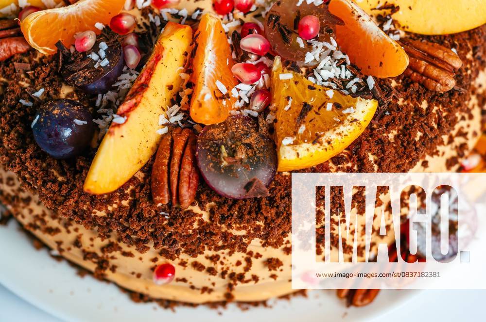 Nahaufnahme eines köstlichen Obstkuchens mit frischen Orangen, Weintrauben und Pekannüssen, perfekt für eine Feier. A beautifully decorated cake with an assortment of fresh fruits, including oranges, grapes, and peaches. The cake is topped with nuts and coconut flakes. (License=RF)