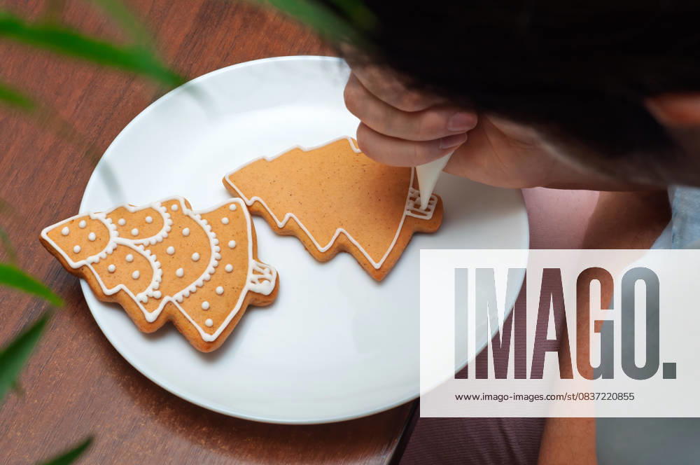 IMAGO Creative, Weihnachten, Food, Backen, Lebkuchen Verzieren von selbstgebackenen Lebkuchen in Form von Weihnachtsbäumen. Hand-piping white icing onto Christmas tree-shaped gingerbread cookies. (License=RF)