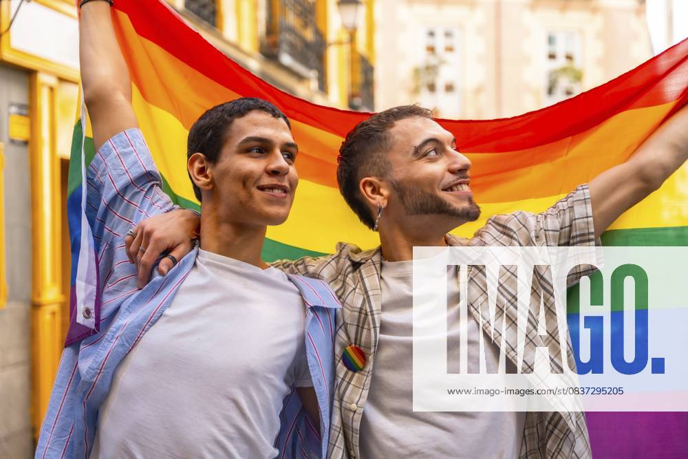 Zwei lächelnde Männer, die sich umarmen und stolz die leuchtende Regenbogenflagge zeigen, die bei einer öffentlichen Demonstration für die Rechte von Lesben und Schwulen, für Liebe und Vielfalt steht Two smiling men embracing and proudly displaying the vibrant rainbow flag, symbolizing lgbtq plus rights, love, and diversity during a public demonstration