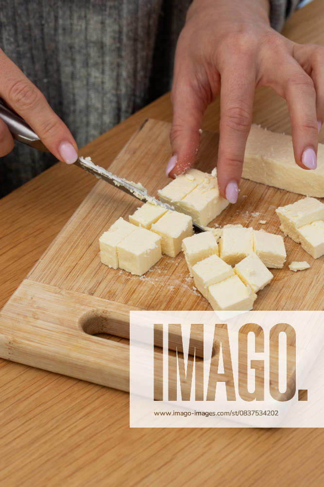 Frauenhände schneiden frischen Feta-Käse auf einem Holzbrett. Molkereiprodukte Female hands cutting fresh feta cheese on a wooden board. Cooking concept, dairy products (License=RF)