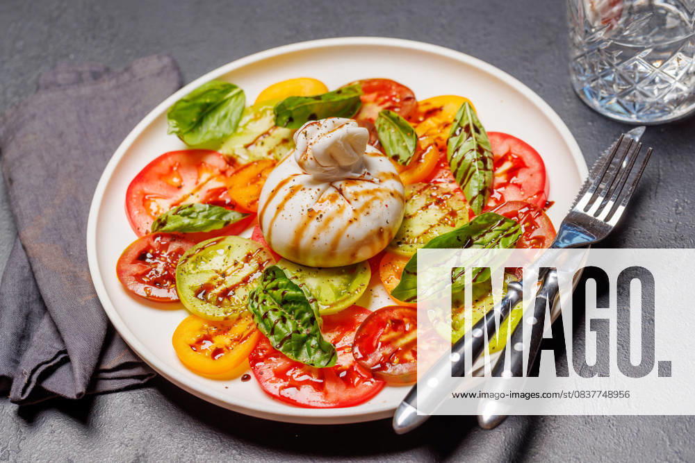 Frische Burrata, serviert auf bunten Tomatenscheiben Fresh burrata served on slices of colorful tomatoes, drizzled with olive oil and herbs (License=RF)