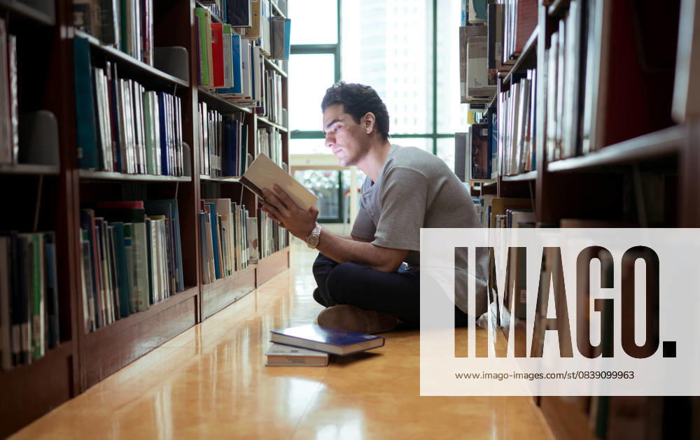 Ein junger Mann sitzt in der Bibliothek und liest konzentriert ein Buch A young man sitting on the library floor reading a book with concentration (License=RF) ,model released, Symbolfoto