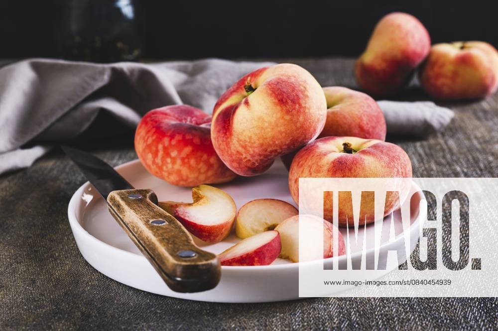 Ganze und geschnittene Pfirsiche und ein Messer werden auf einen Teller auf dem Tisch gelegt Whole and sliced peaches and a knife are placed on a plate on the table