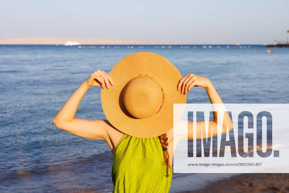 Frau hält Strohhut über das Gesicht am sonnigen Strand Woman holding straw hat over face on sunny beach. (License=RF) ,model released, Symbolfoto