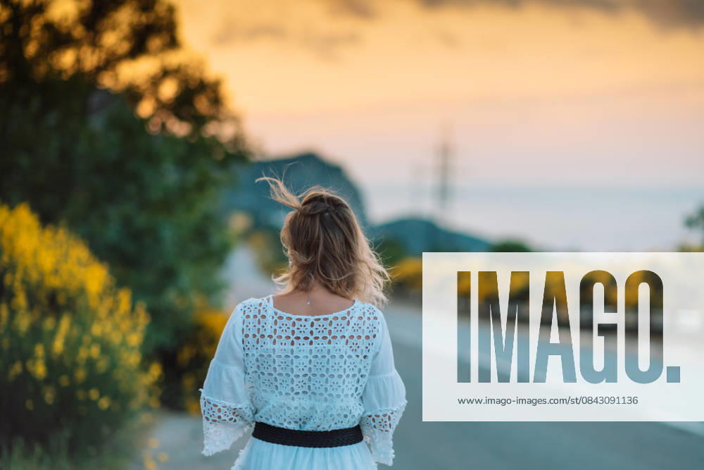 A woman is walking down a road with a yellow bush in the background A woman is walking down a road with a yellow bush in the background. The sky is orange and the sun is setting, model released, , 61517538.jpg RECORD DATE NOT STATED