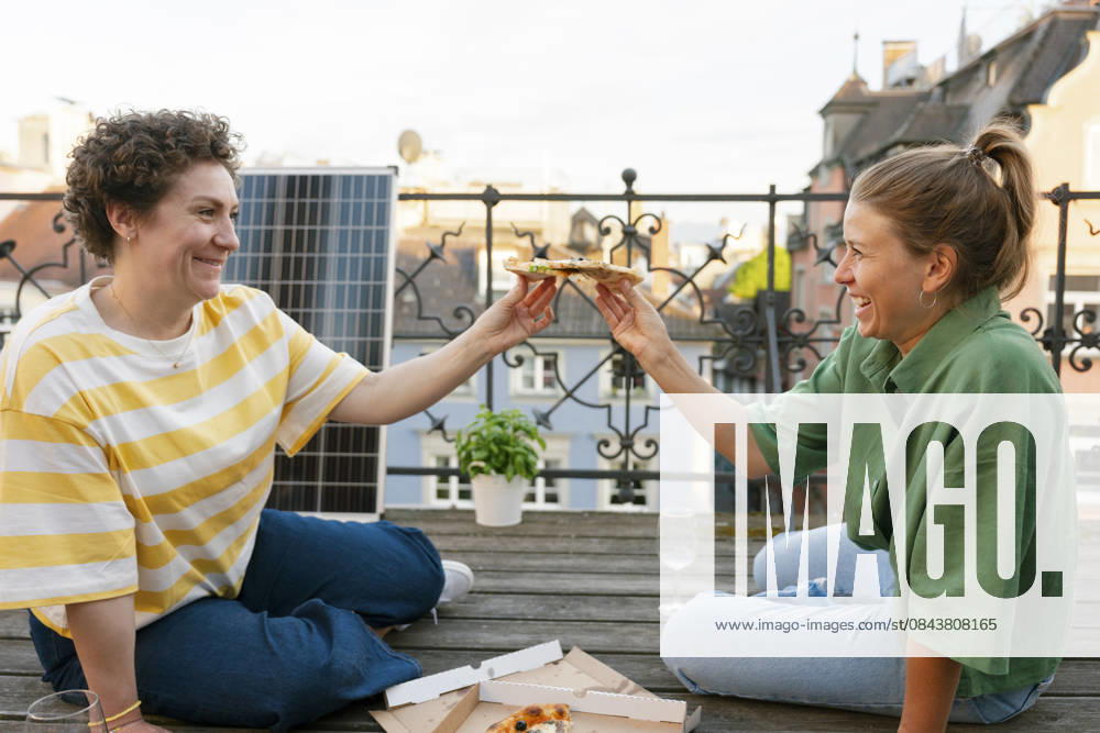 Smiling friends enjoying pizza on urban terrace with solar panel model released, Symbolfoto, FLMZF00915