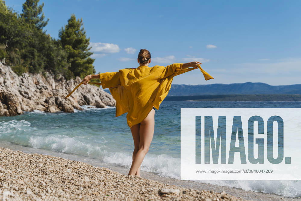 Woman in yellow cape enjoying playful moment by the sea on beach model released, Symbolfoto, NDEF03193