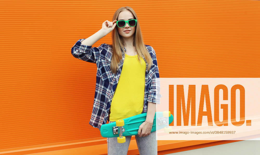 Stilvolle junge Frau mit Skateboard, modernes Teenager-Mädchen posiert auf der Stadtstraße Stylish young woman standing with skateboard in colorful clothes, cool modern teenage girl posing on orange background (License=RF) ,model released, Symbolfoto