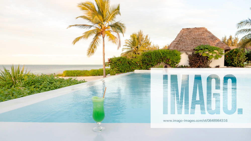 Honeymoon paradise at a Zanzibar resort pool A refreshing green cocktail by the pool at a luxurious Zanzibar resort. The serene background includes palm trees and a thatched villa, reflecting paradise. Model Released SilviaRedondo_ID33141_1127807_025