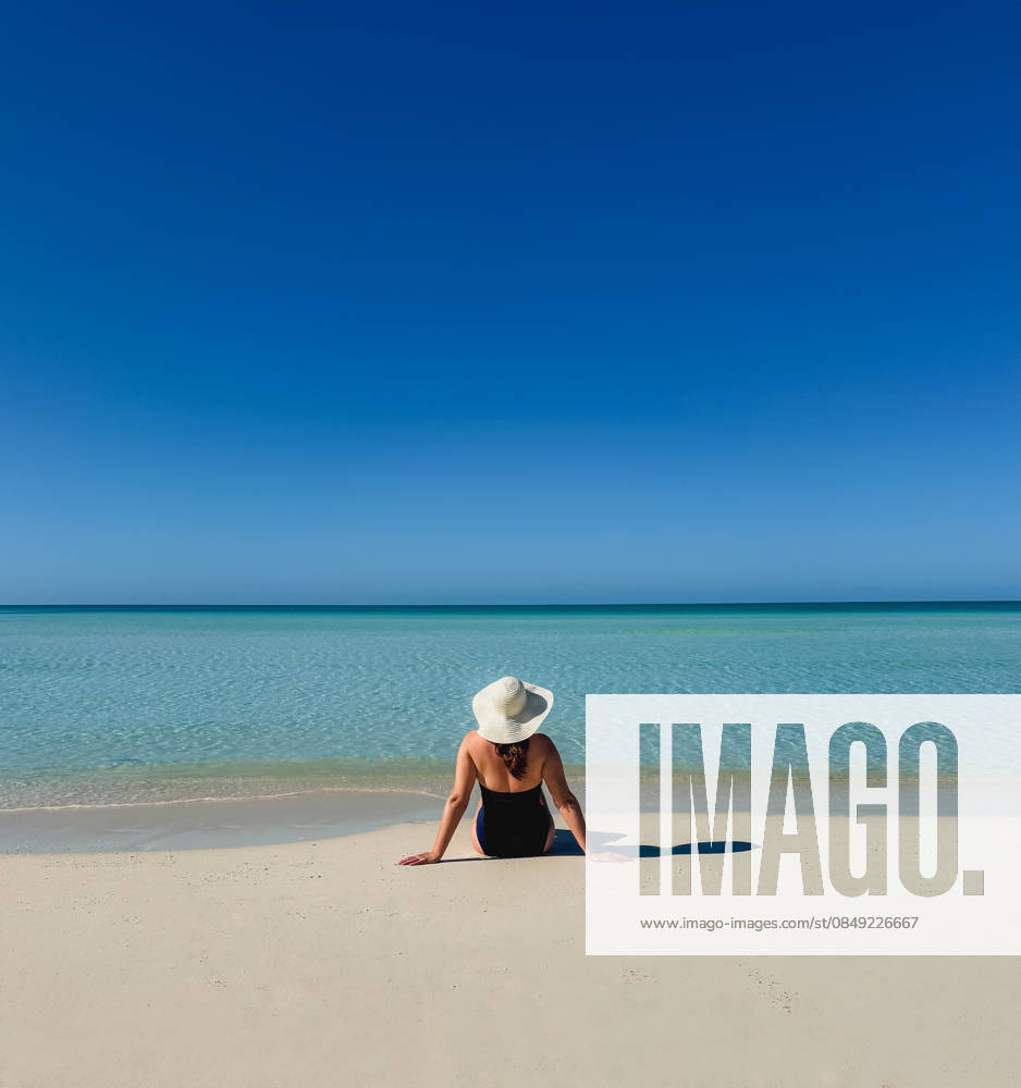 Woman in swimsuit sunhat sitting on tropical beach looking at ocean. Grace Bay, Caicos Islands, Turks and Caicos Islands CR_DOHO26022882-1973352-01 ,model released, Symbolfoto