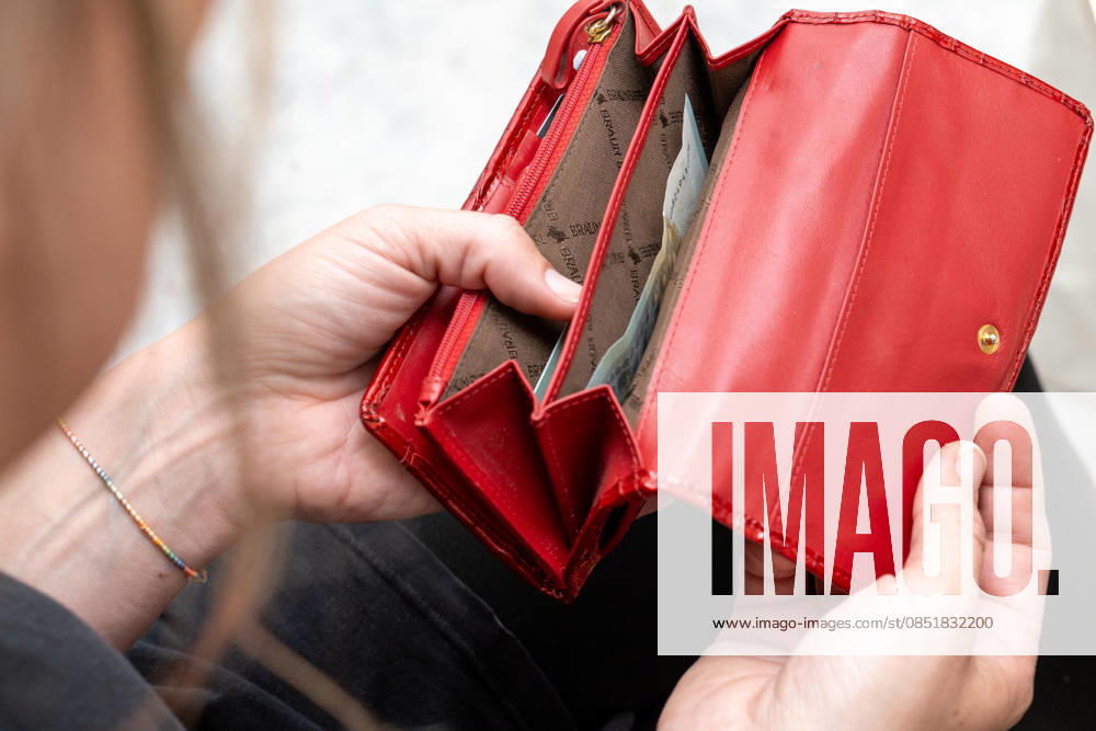 A woman looks into her almost empty purse, symbolizing the rising cost of living, inflation and financial worries in everyday life