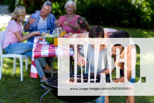 Father teaching son cooking on barbecue with family Father teaching son cooking on barbecue with family in background, model released, , property released, Cape Town, South Africa, 26.01.2016, 717137.jpg, mother, father, son, daughter, enjoying, relaxing, leisure, spare time, free time, activities, time off, together, childhood, smiling, happiness, bonding, love, cute, casual, lifestyle, kid, summer, fun, playful, multi-generation family, grandmother, grandfather, grandson, granddaughter, granny, granddad, relaxation, meal, food and drink, barbecue, grilling, barbecue grill, holding, breakfast, retirement, golden years 50s, Mature Adult, Man, Male, Caucasian, 60s, Senior, Elderly, 20s, Young Adult, Child, Girl, Female, Boy, 30s, Mid Adult
