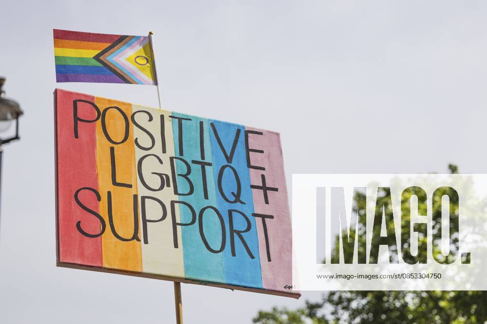 Aufmunterndes Regenbogenplakat mit der Aufschrift Positive LGBTQ Unterstützung mit einer Progress Pride Flagge, die Verbündete, Gleichheit und Inklusion bei einer friedlichen Parade oder Gemeinschaftskundgebung symbolisiert Uplifting rainbow placard reading Positive LGBTQ Support with a Progress Pride flag, symbolizing allyship, equality and inclusion at a peaceful parade or community rally