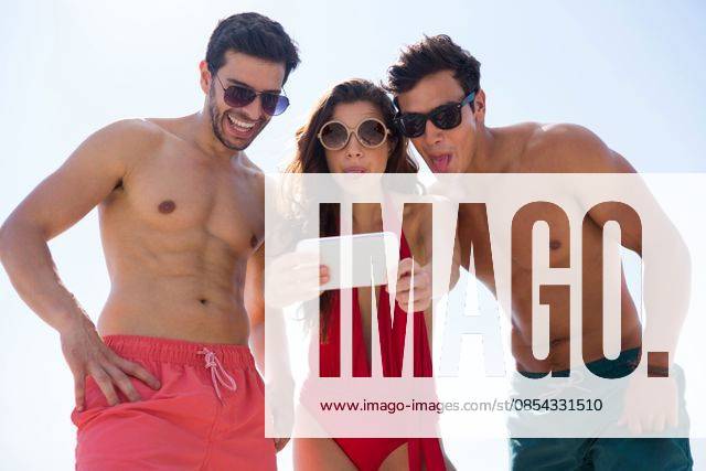 Low angle view of young friends taking selfie against clear sky Low angle view of young friends taking selfie through mobile phone against clear sky at beach, model released, Cape Town, South Africa, 17.01.2017, 979470.jpg, friend, friendship, selfie, mobile phone, clear sky, beach, happy, sunglasses, sunny, holding, making a face, sticking out tongue, standing, side by side, sunlight, shirtless, shorts, together, bonding, enjoyment, fun, happiness, vacation, weekend activities, lifestyle, leisure, summertime, bright, beachwear, bikini, protection, safety, swimsuit, swimwear, red, hand on hip, connection, wireless, cellphone, smartphone, wireless technology, photographing, photography themes Outdoors,Front view,Low angle view,Focus on For