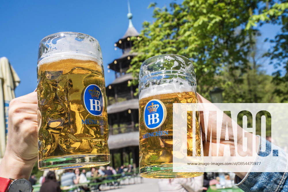 Beer garden at the Chinese Tower, spring day in the English Garden, two guests toast with their mugs of beer, Munich, April 2026 Germany, Munich, April 22, 2026, Beer garden at the Chinese Tower, spring in the English Garden, temperatures up to 16 degrees, many enjoy the sun with beer and a snack, two guests toast with their mugs, everythi