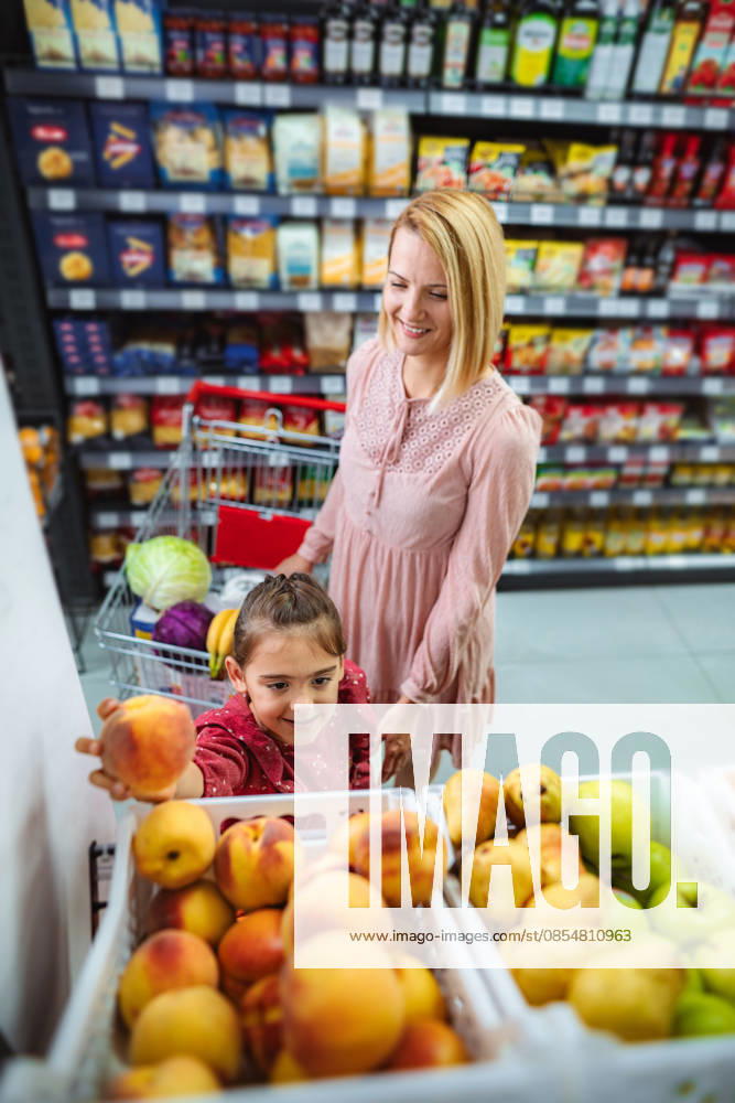 Mutter und Tochter suchen im Supermarkt frische Pfirsiche aus Mother and daughter smiling, choosing fresh fruit from a display in a grocery store (License=RF) ,model released, Symbolfoto