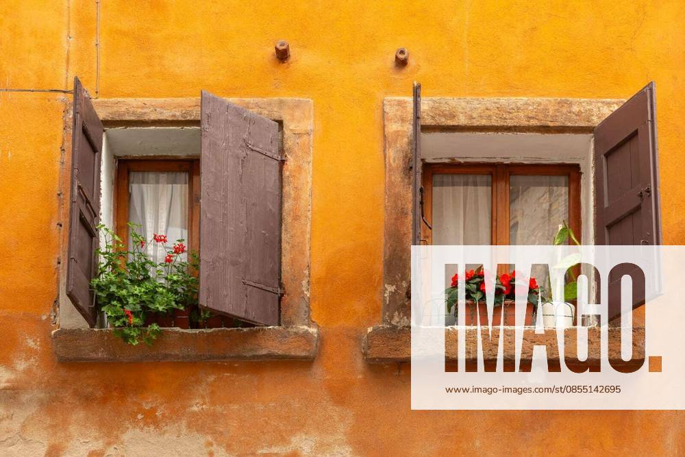 Two old windows with wooden shutters and flower pots on orange facade in Verona, Italy.