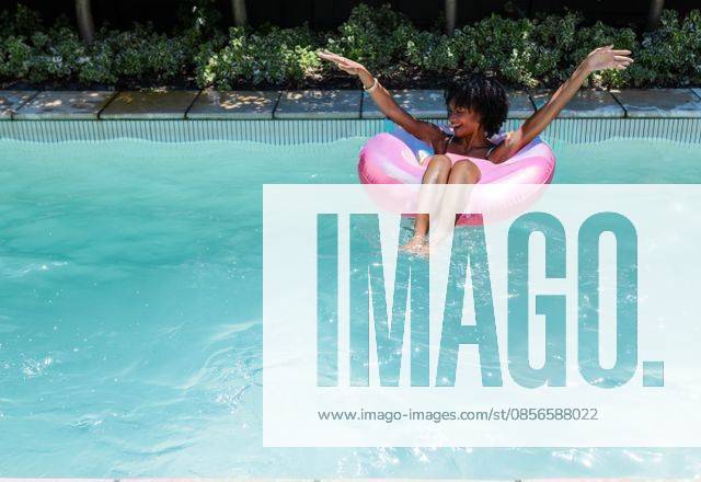 African American woman floating on pink donut float in blue pool wearing bikini, copy space, model released, property released, 26.02.2025 06:00:00, 13157771