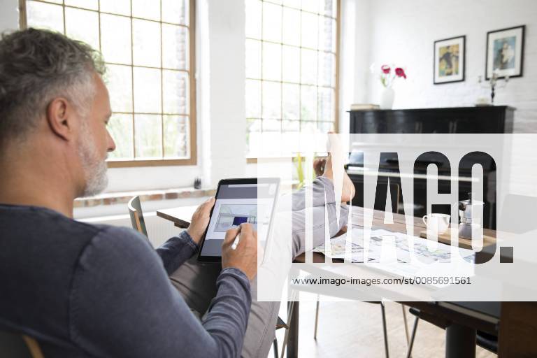 Mature man working from his home office with feet up, using tablet model released Symbolfoto property released FKF03042