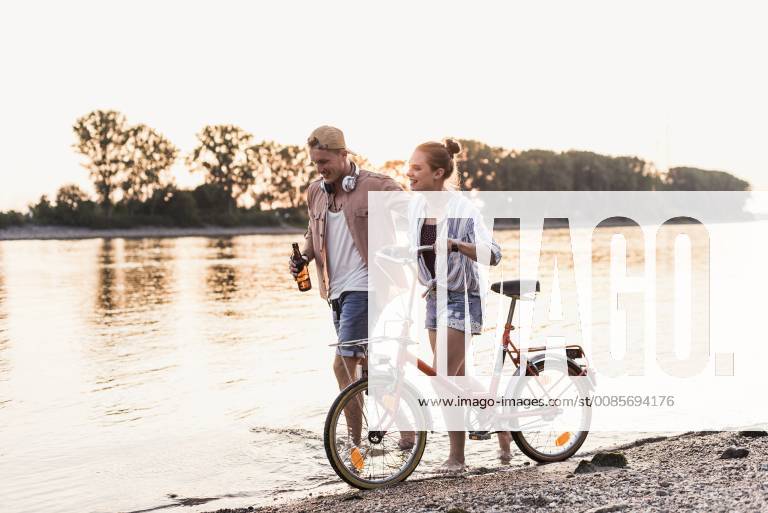 IMAGO Creative: Sommer, Abendspaziergang Young couple with bicycle wading in river model released Symbolfoto UUF11559