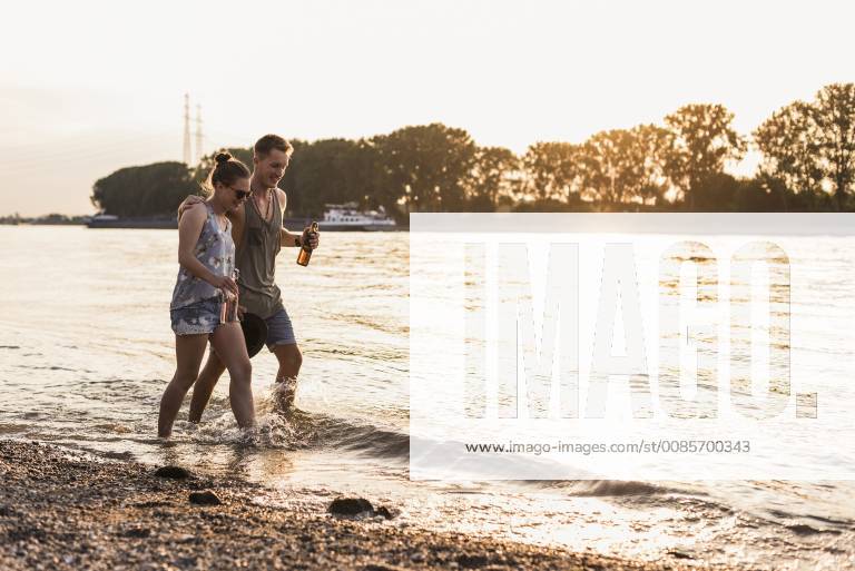 IMAGO Creative: Sommer, Abendspaziergang Happy young couple wading in river at sunset model released Symbolfoto UUF11546