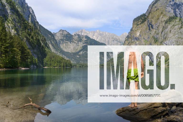 Young man in swimming trunks stands on a stone in the Obersee mountain lake mountain landscape behind Watzmannmassiv Salet am Königssee National Park Berchtesgaden Berchtesgadener Land Upper Bavaria Bavaria Germany Europe
