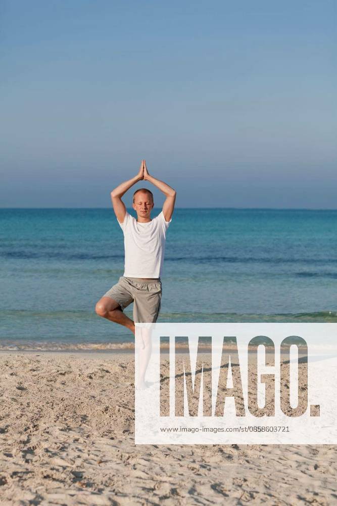 Young sporty man doing sport yoga on the beach in the sand by the sea in the sun model released Symbolfoto