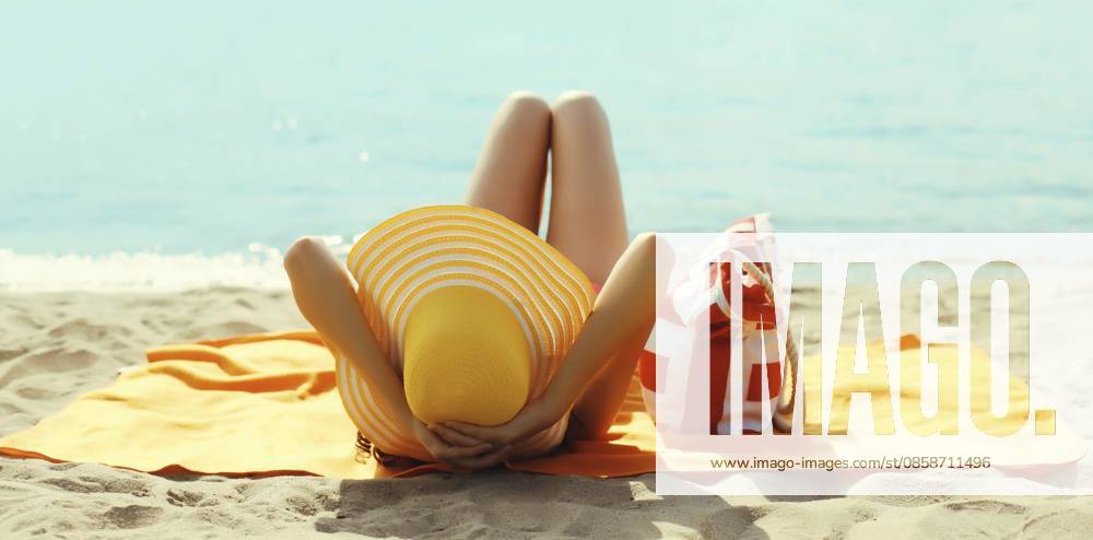 Sommerurlaub, schöne glückliche, entspannende junge Frau mit gelbem Strohhut und Tasche, die auf Sand am Meeresstrand liegt Summer vacation, beautiful happy relaxing young woman with yellow straw tourist hat with bag lying on sand on sea beach